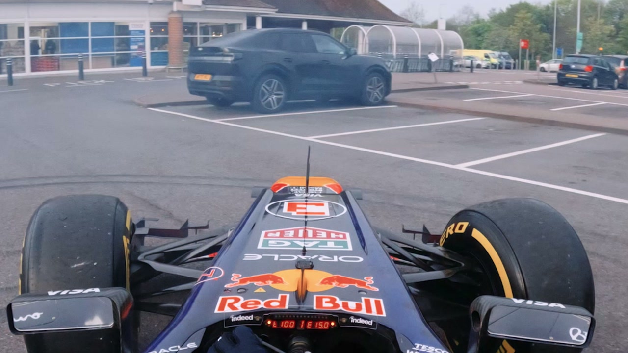 Red Bull Formula 1 car at speed past a Tesco car park